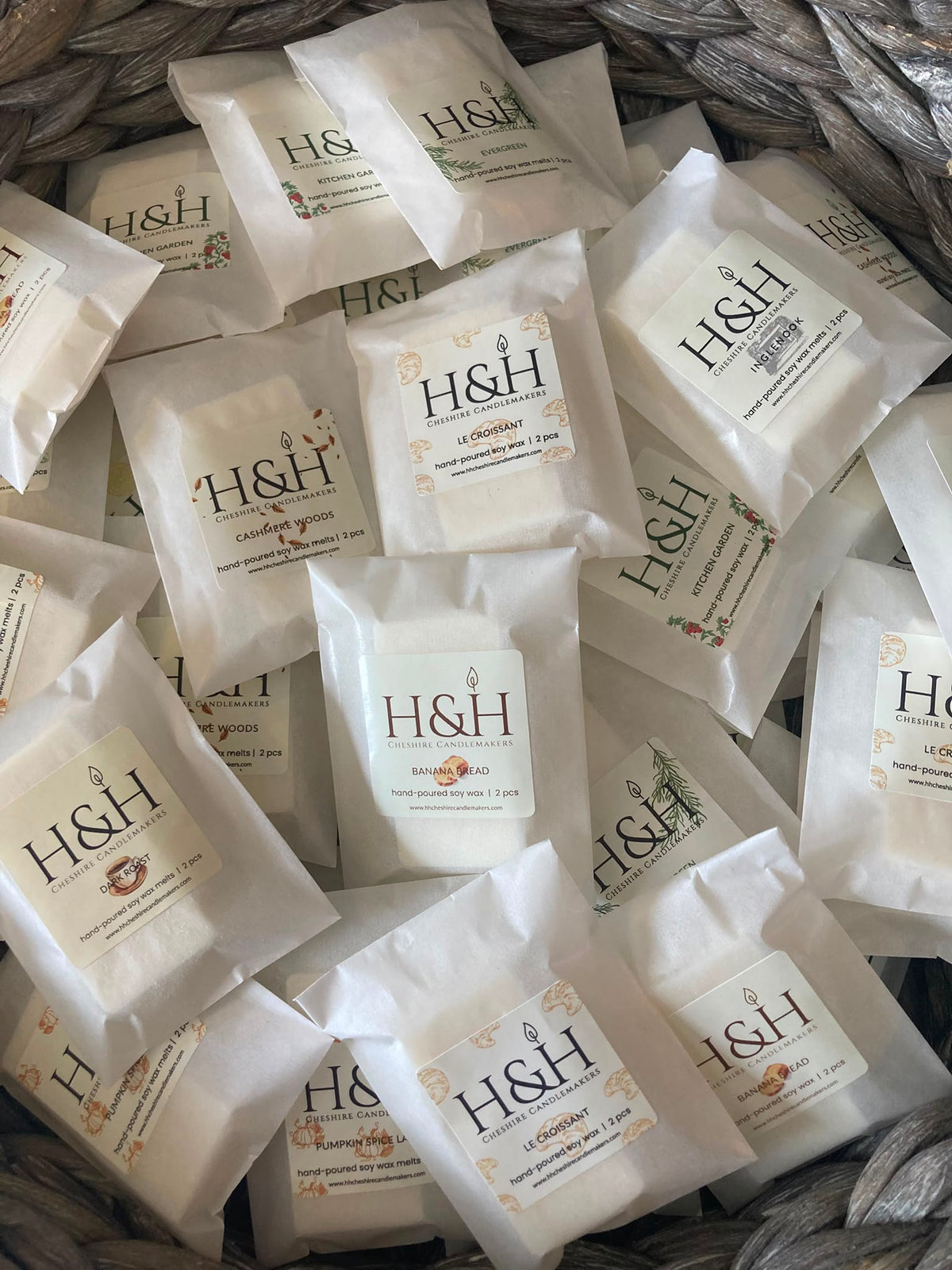 Multiple small white H&H branded sachets or packets arranged in a woven basket. The packets have white labels with black H&H lettering and small decorative text.